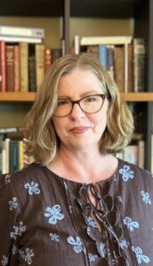 woman with shoulder-length hair and glasses standing in front of bookshelves