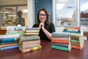 woman with glasses sits with stacks of books in front of her