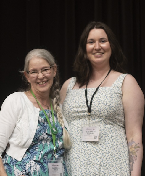 two women stand by side, one with long hair and glasses