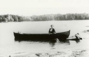 black and white image of a woman in dark clothing in a canoe on a small lake